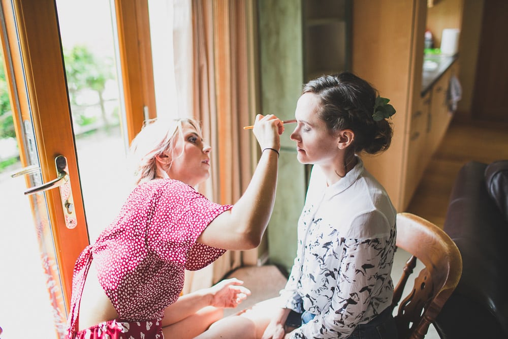 friend makes make up to bride in farm countryside wedding east sussex UK