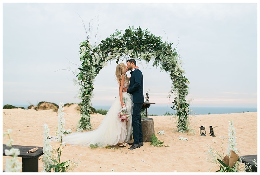 couple with flower arch backdrop at the sand dunes during elopement at Areias do Seixo