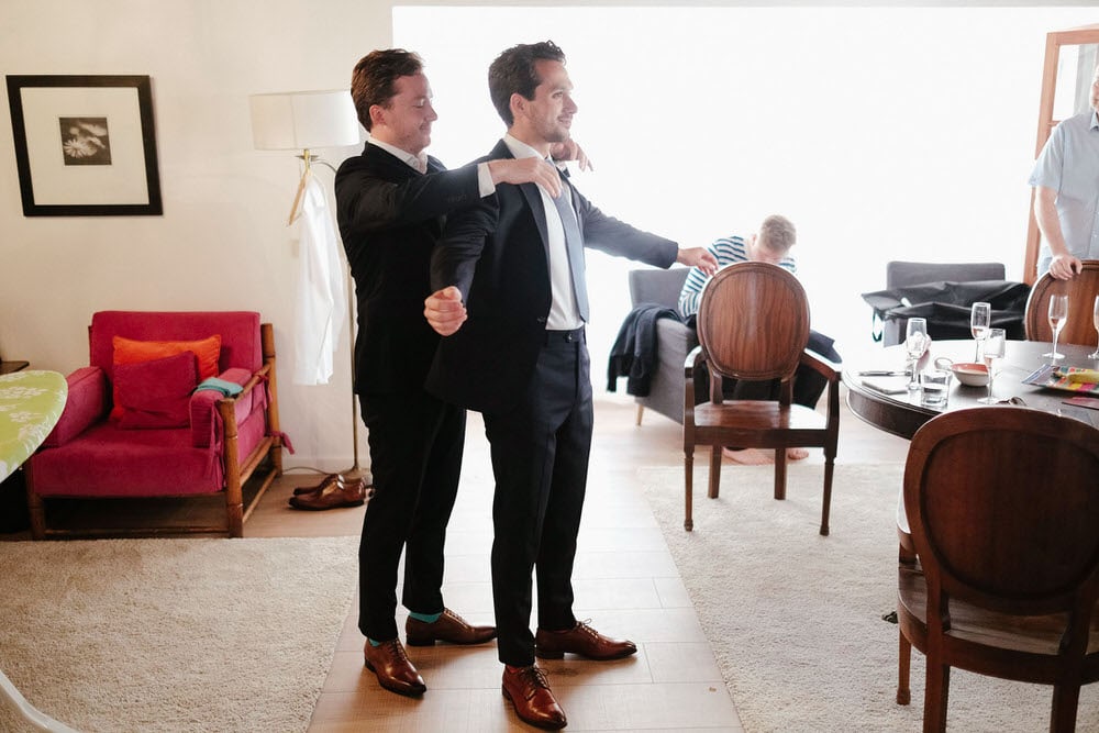 The bestman helping the groom put on his jacket in a rustic and colorful room