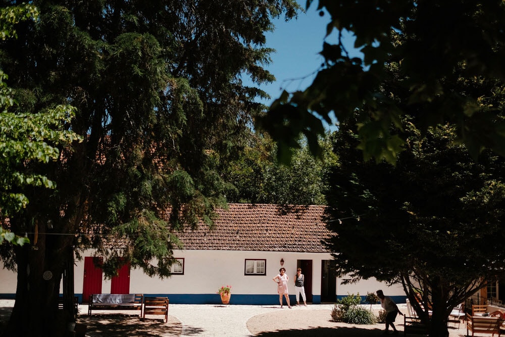 A typical Portuguese quinta patio surrounded by trees, guests seen in the background in front of the big house on a sunny day