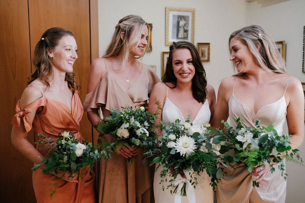 A fun moment of the bridesmaids and bride laughing together, while holding their bouquets and showing their happiness before the ceremony