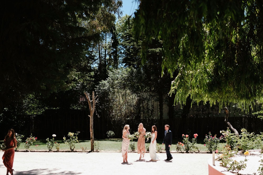 The bride walks with her bridesmaids to the altar, walking through a lush garden surrounded by big trees