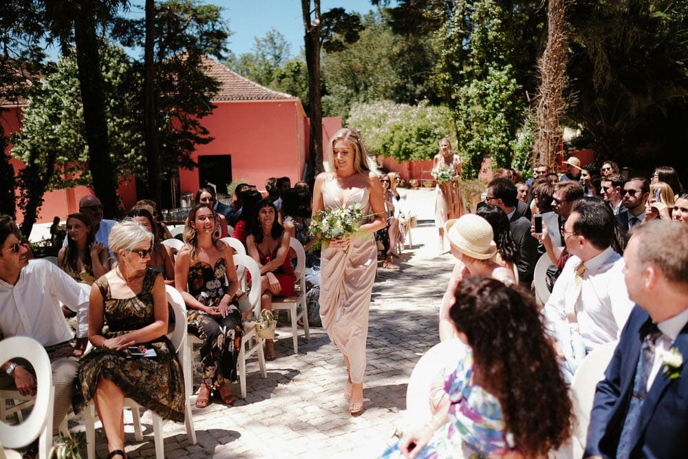 The bridesmaids walk towards the altar, holding their flowers in front, as all the guests enjoy watching them walk towards the altar