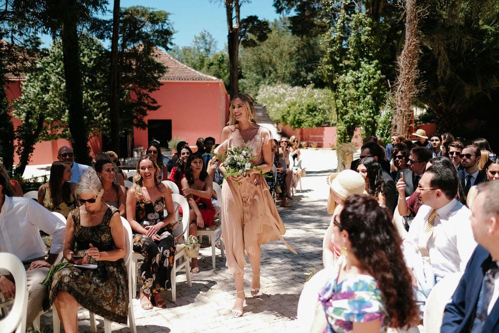 The bridesmaids walk towards the altar, holding their flowers in front, as all the guests enjoy watching them walk towards the altar