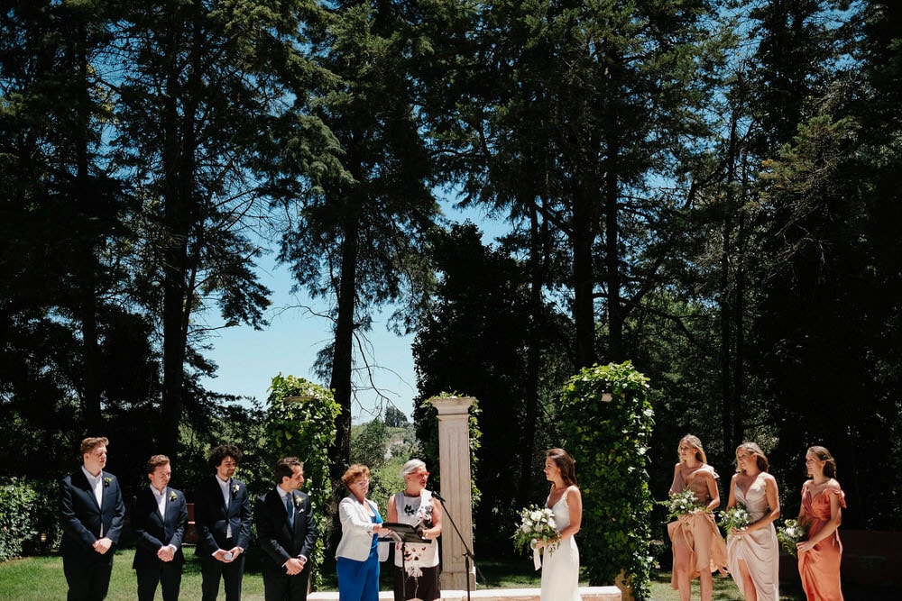 The wedding party stands in formation around the couple, with a typical American wedding scene to one side, girls on one side and boys on the other, with the celebrant in the middle with the couple