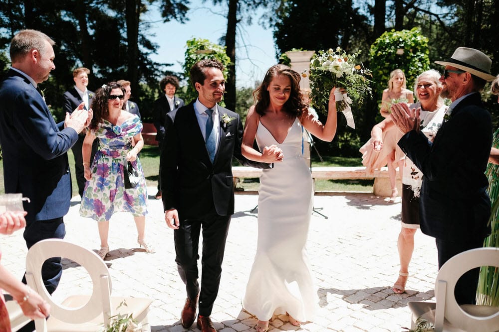 Quinta da Bichinha rustic destination wedding . The bride and groom walk out of the ceremony, with guests clapping, as she raises her bouquet in a sign of victory and joy