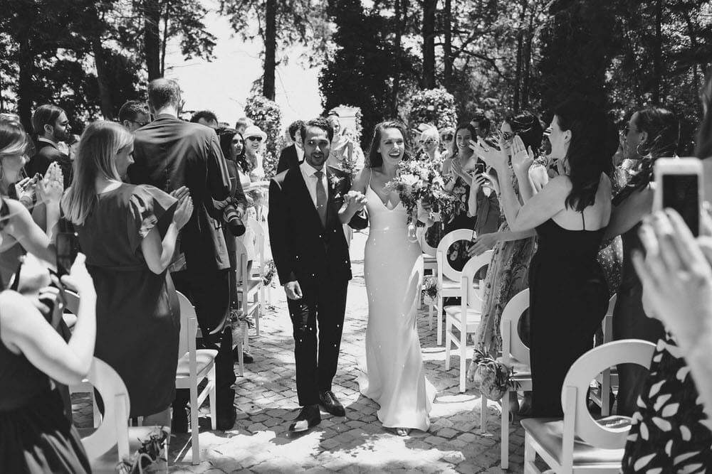 In black and white, the bride and groom walk, greeting guests in the aisle after the ceremony at quinta da bichinha.