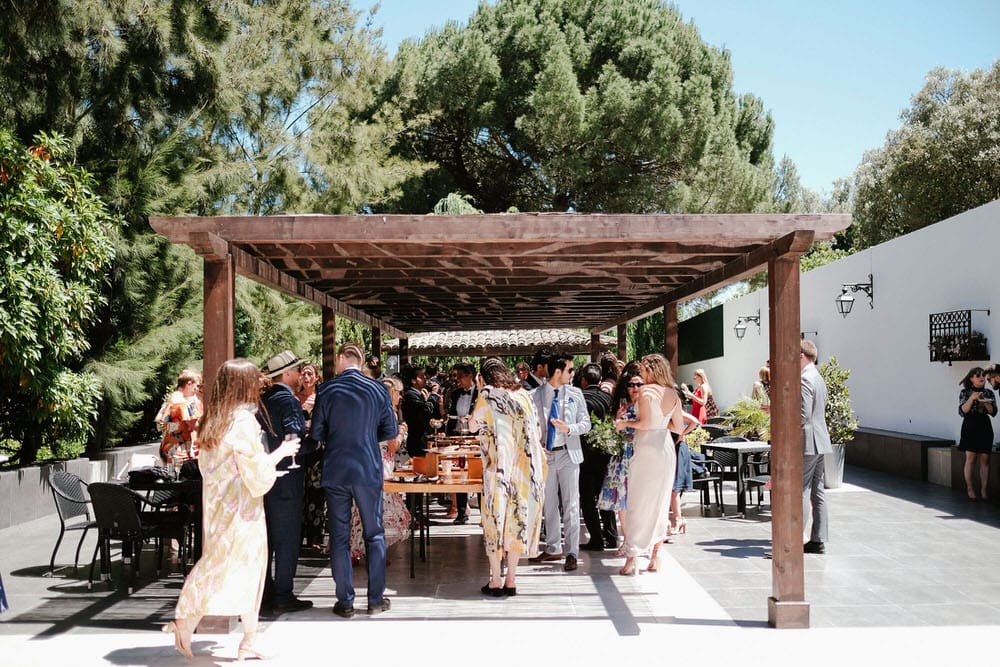 Cocktail hour with guests enjoying food and drink under the shade in a large solid wood pergola