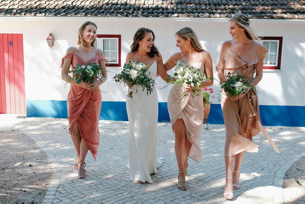Candid moment of the bride and her bridesmaids walking with flowers in an elegant pose in front of the Portuguese facade at Quinta da Bichinha