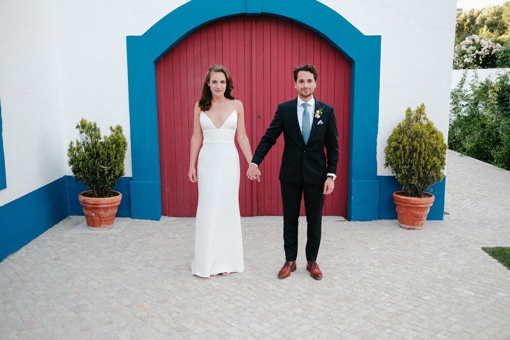 The groom and bride stand in front of a red door with a blue frame on the Portuguese facade
