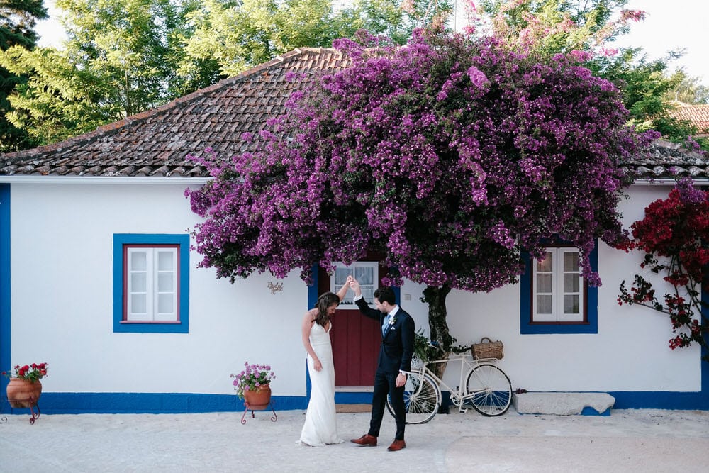 Quinta da Bichinha rustic destination wedding . The groom and bride dance under a beautiful bougainvillea and a rustic bicycle in white, blue, and red colors of the quinta da bichinha with the typical Portuguese facade