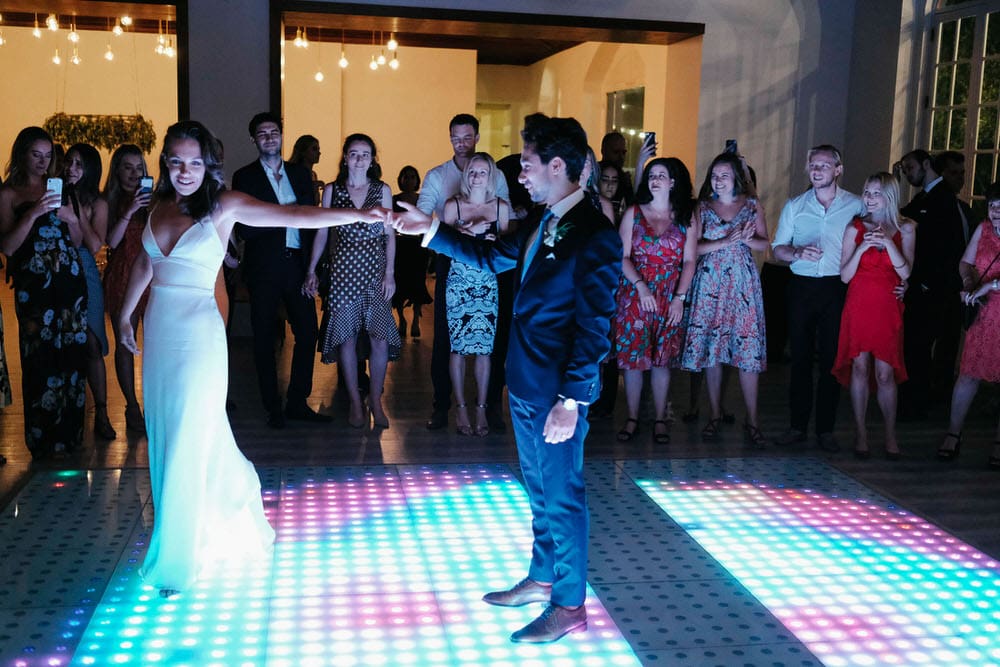 The bride gracefully extends her arm, showcasing the beauty of her dress during the first dance of the newlyweds on the LED dance floor at Quinta da Bichinha