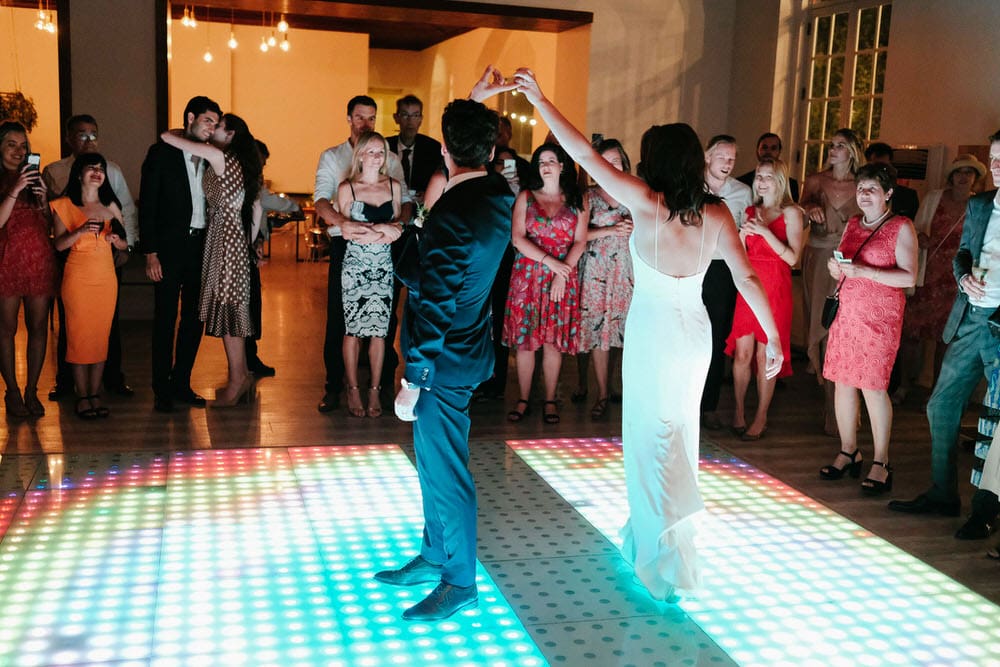 The bride gracefully extends her arm, showcasing the beauty of her dress during the first dance of the newlyweds on the LED dance floor at Quinta da Bichinha