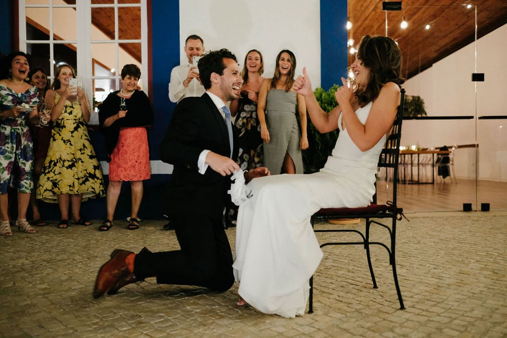 The groom removes the garter with his mouth in front of a giggling crowd of guests