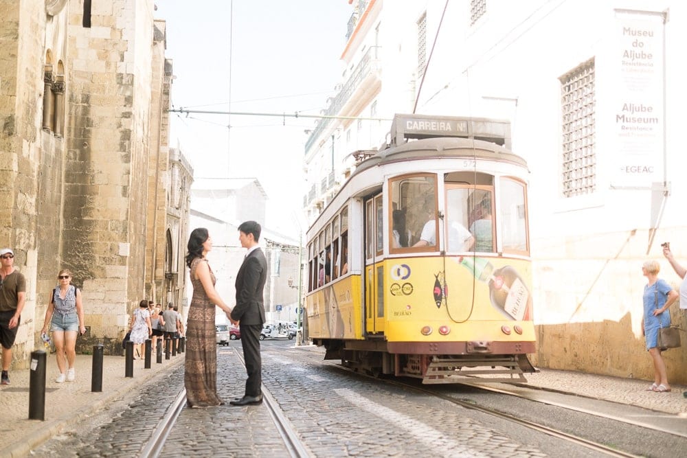 asian american couple with facin each other on medieval street in LIsbon with tram passing close them